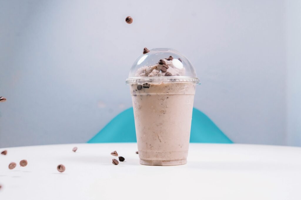 A delicious iced chocolate milkshake topped with chocolate chips and a clear dome lid on a table.