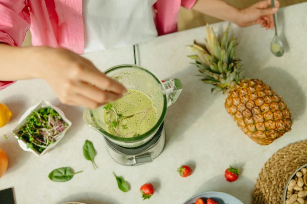 Top view of a green smoothie being prepared with pineapple and greens on a countertop.